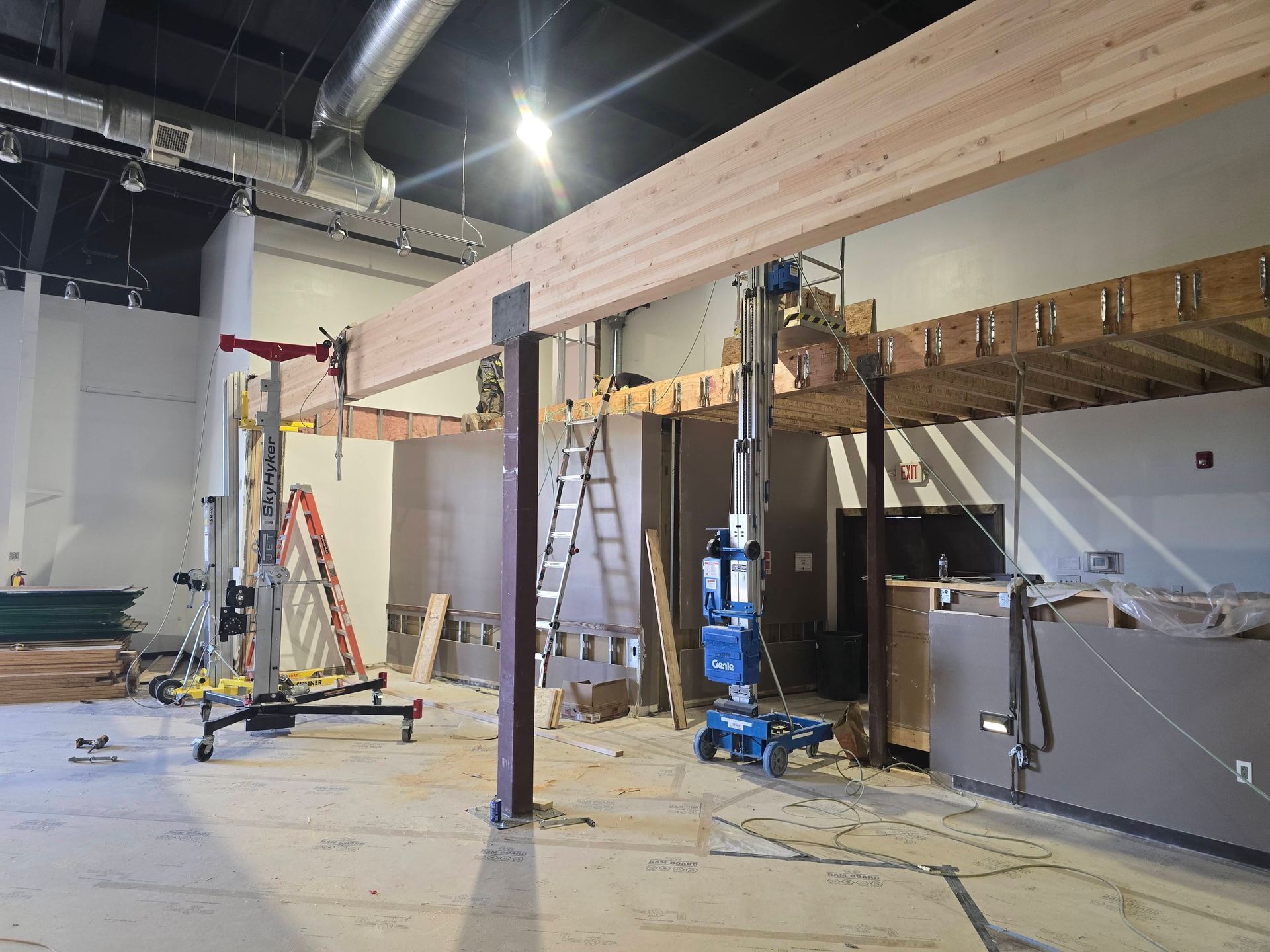 Construction site with wooden beams being installed, ladders, and lift equipment in an unfinished interior space