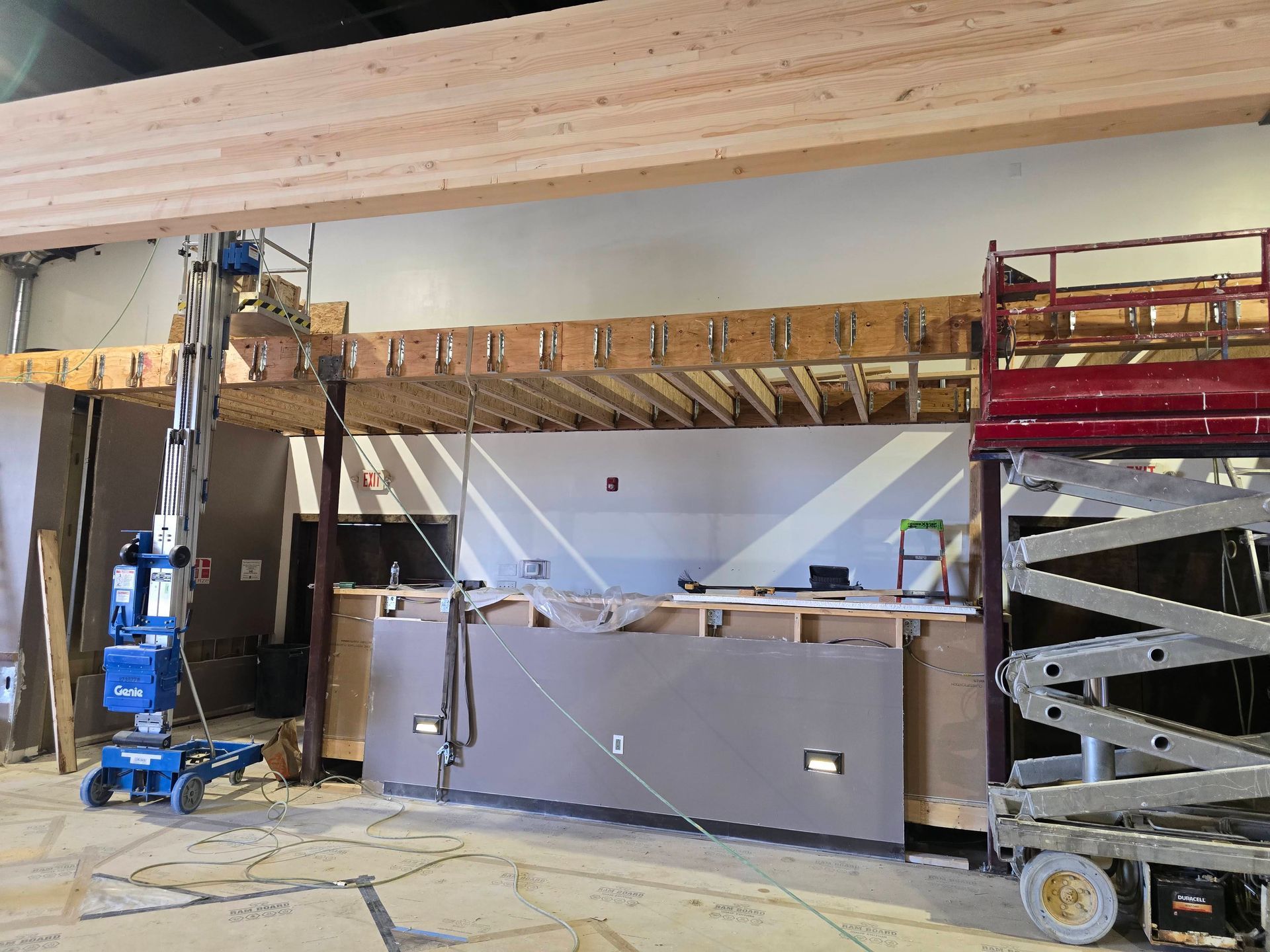 Construction lift and scaffold inside a building under renovation, with equipment and a wooden beam overhead