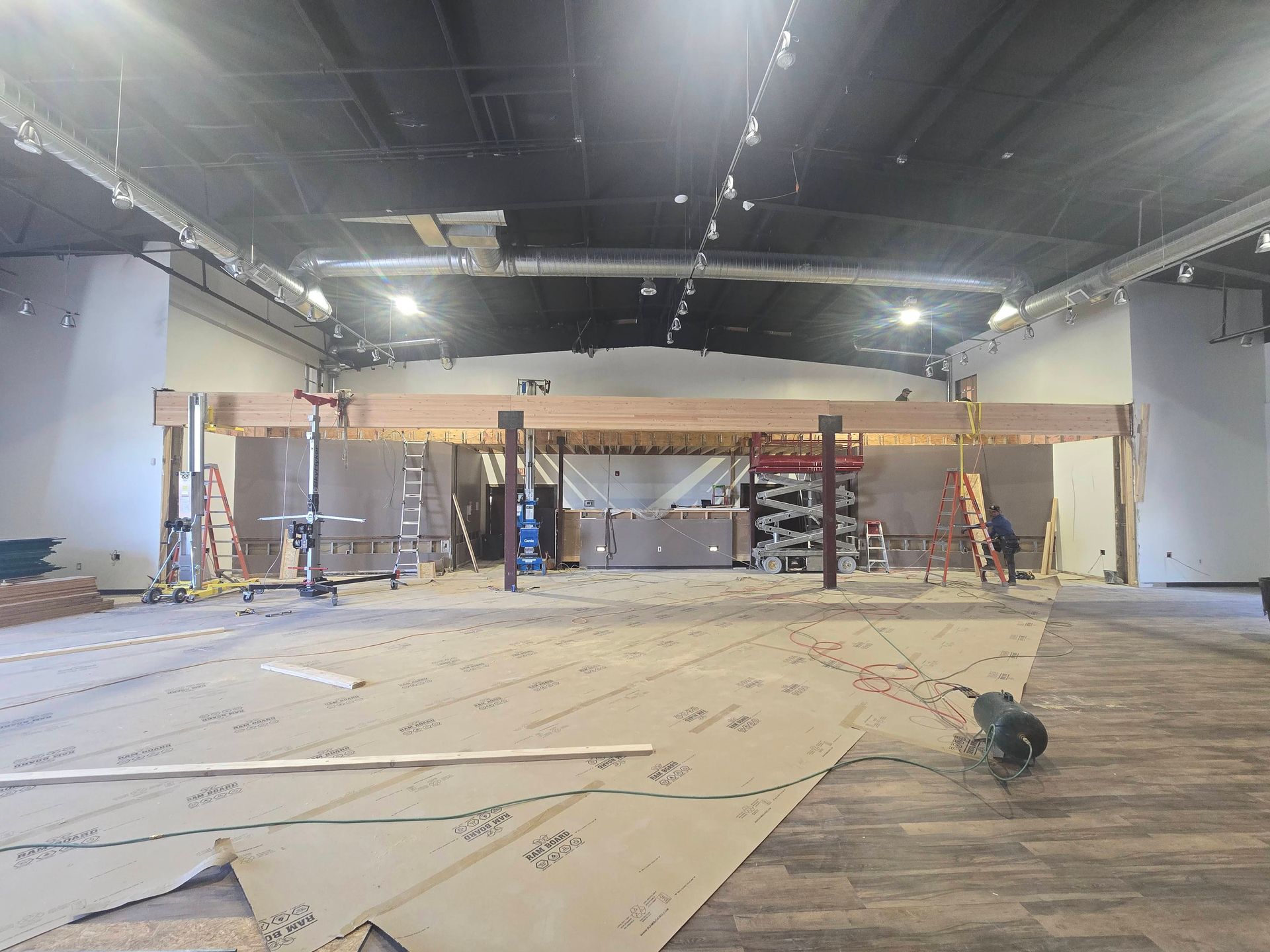 Empty indoor warehouse or studio under renovation, with scaffolding, tools, and plywood sheets on the floor.