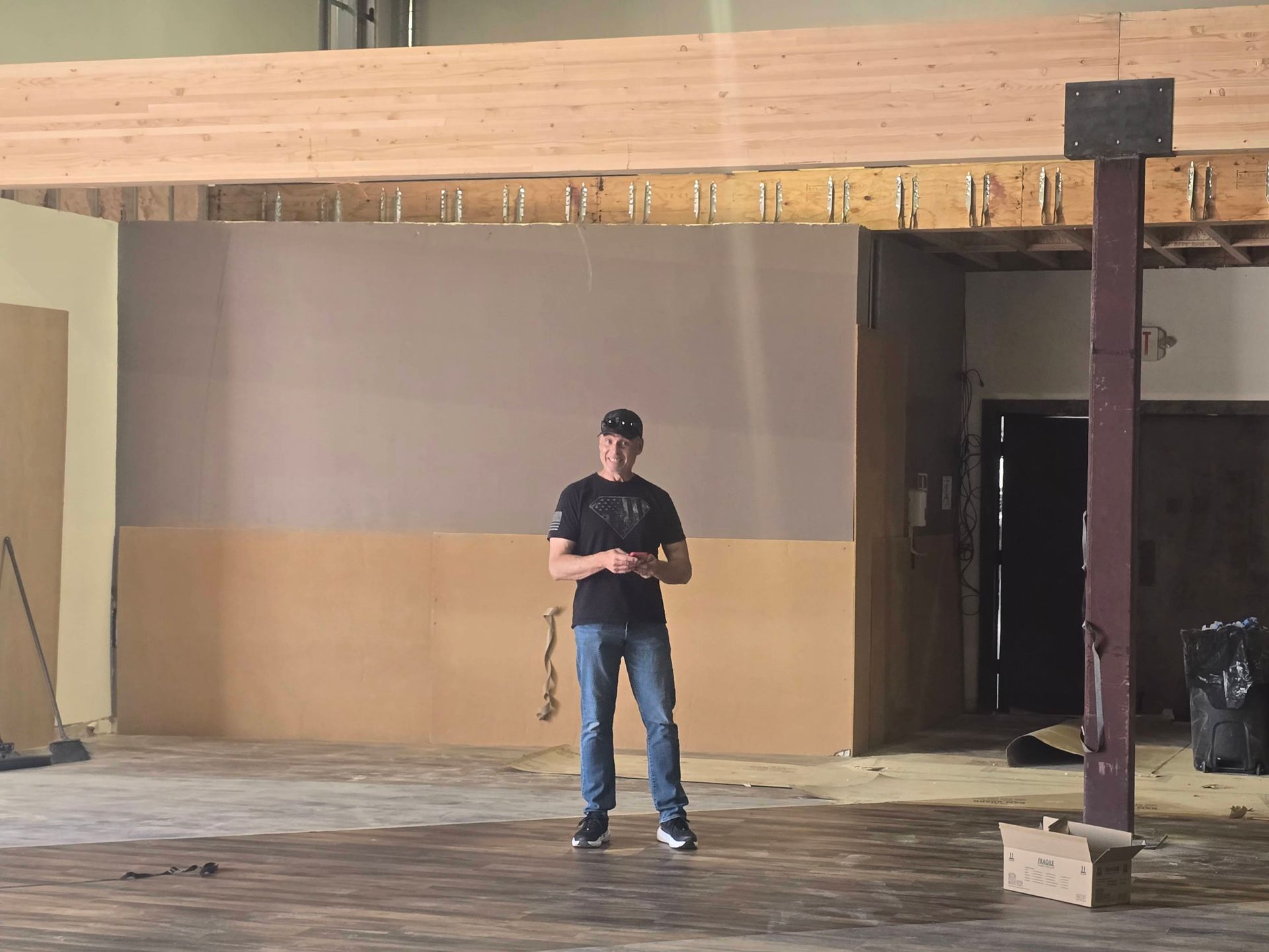Person standing in a large unfinished room, holding a cable under a wooden beam structure.
