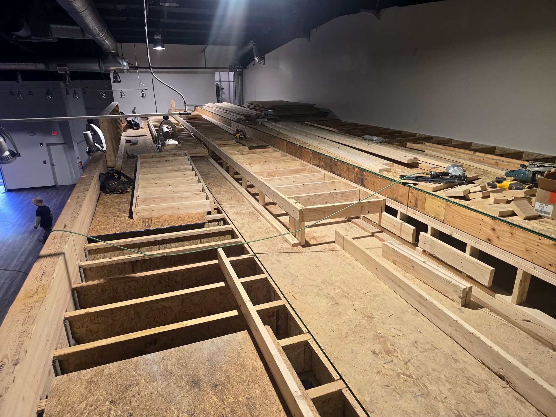Wood-framed platform under construction in a large indoor room with tools and exposed beams
