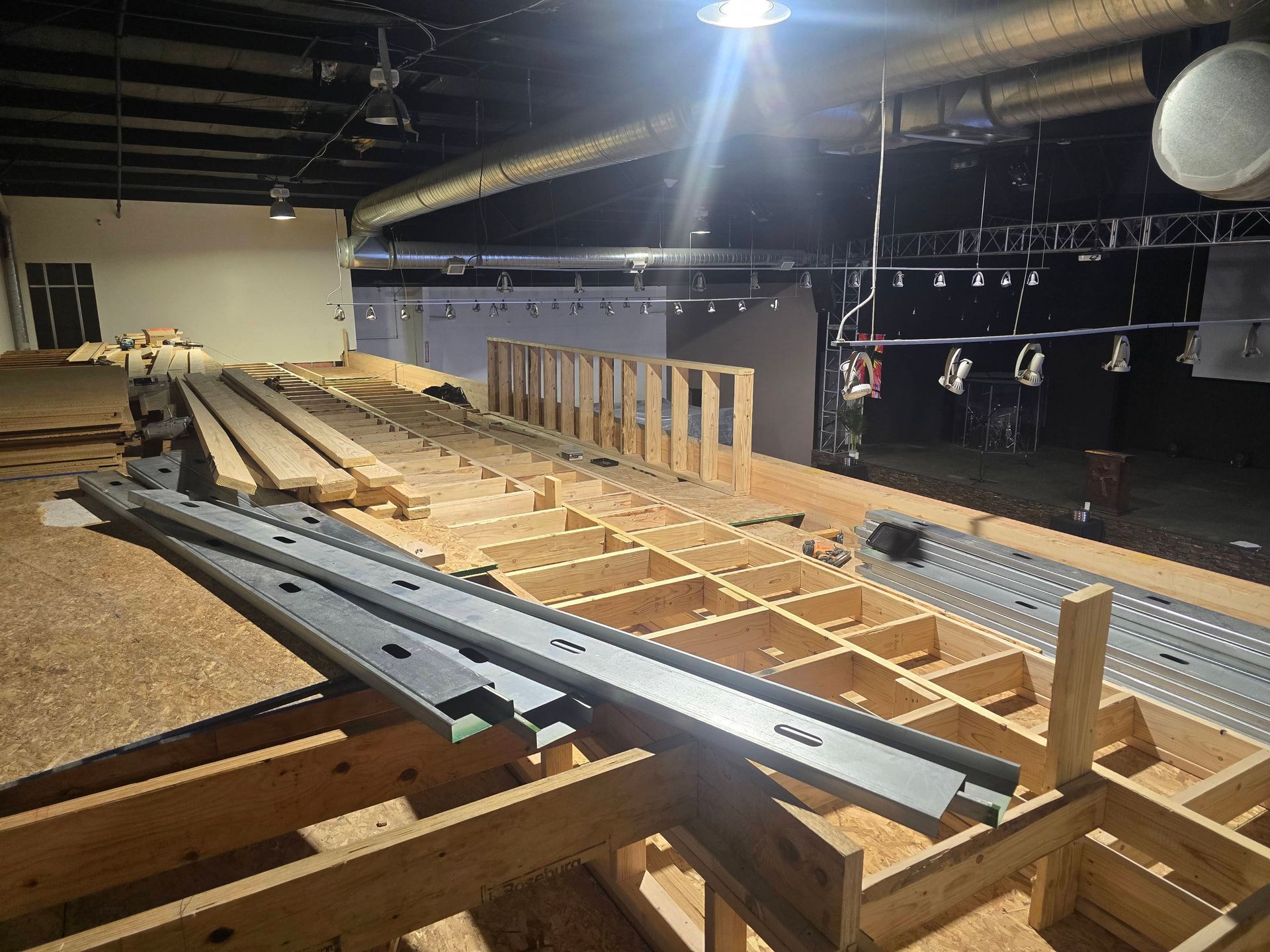 Indoor construction area with wooden floor framing and stacked metal beams under dim lighting