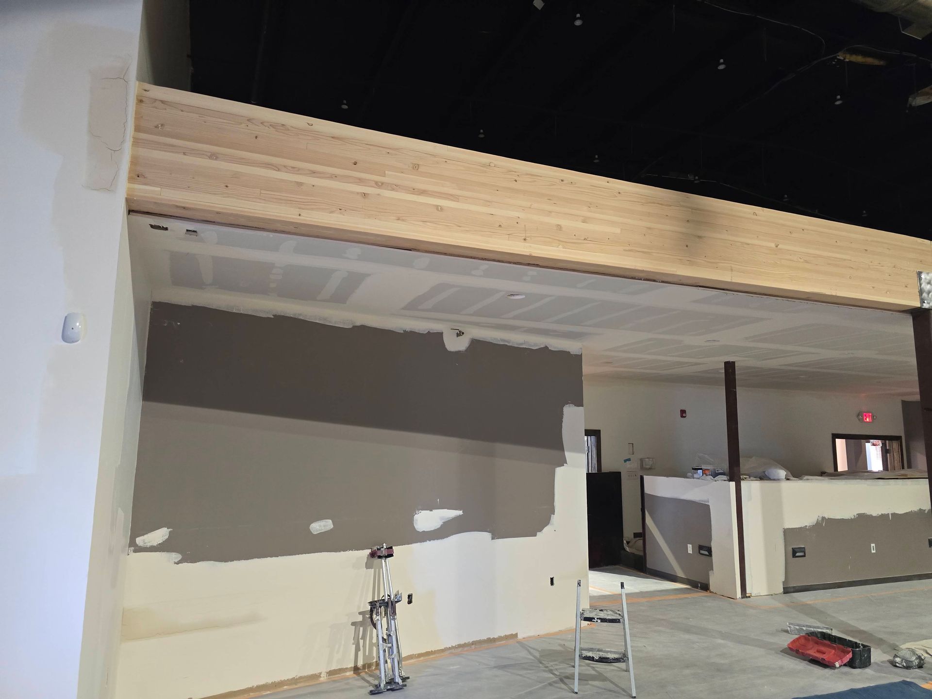 Interior under construction with a raised wooden loft, unfinished drywall, and equipment on the floor.