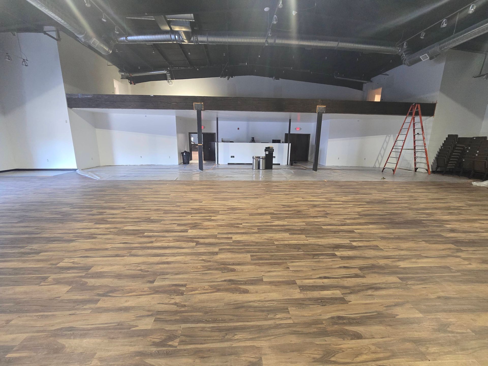 Empty indoor hall with wood-look flooring, white walls, and a ladder near the back wall.