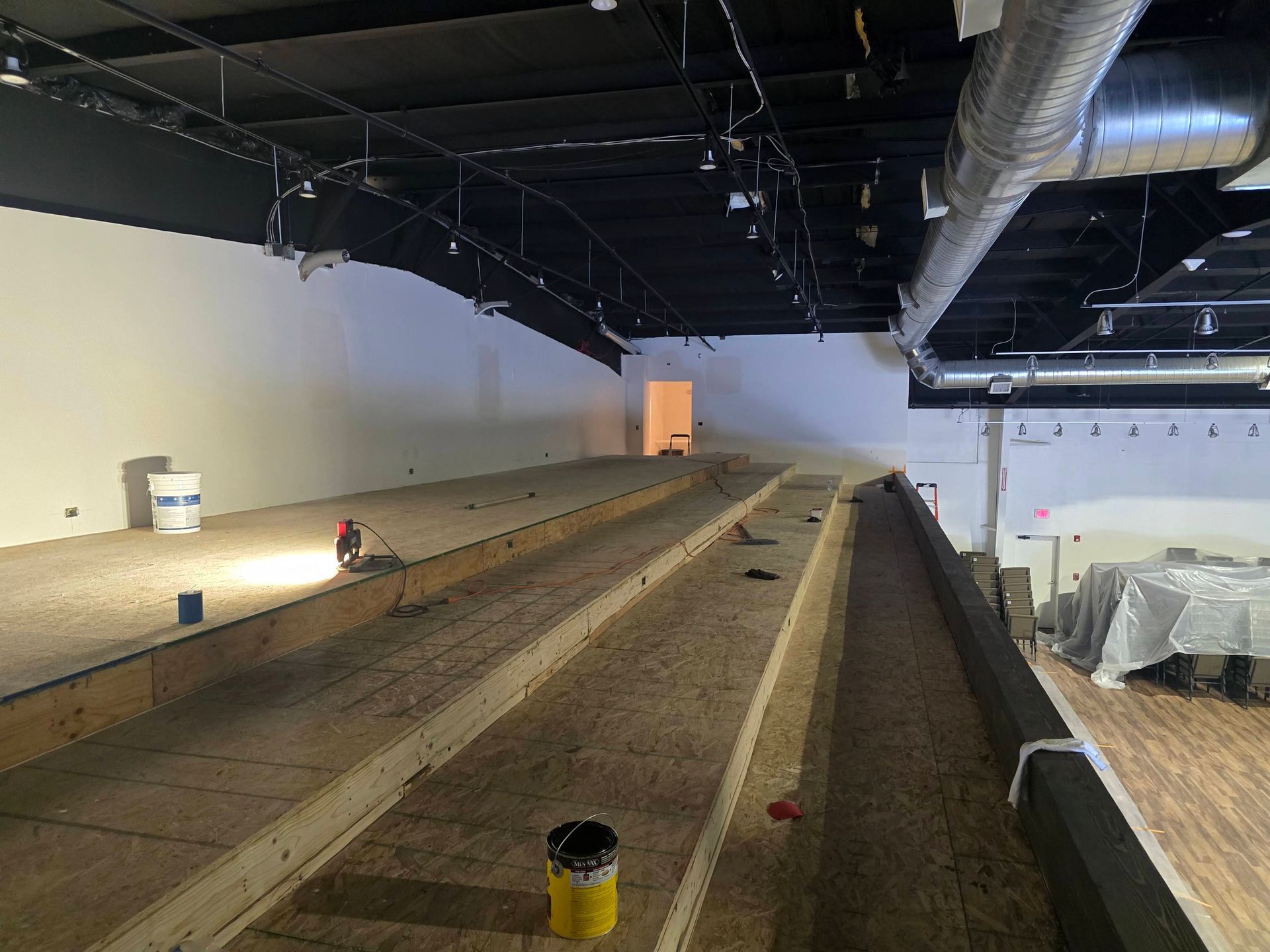 Indoor construction site with long dirt trench, exposed black ceiling ducts, and work lights along the walls