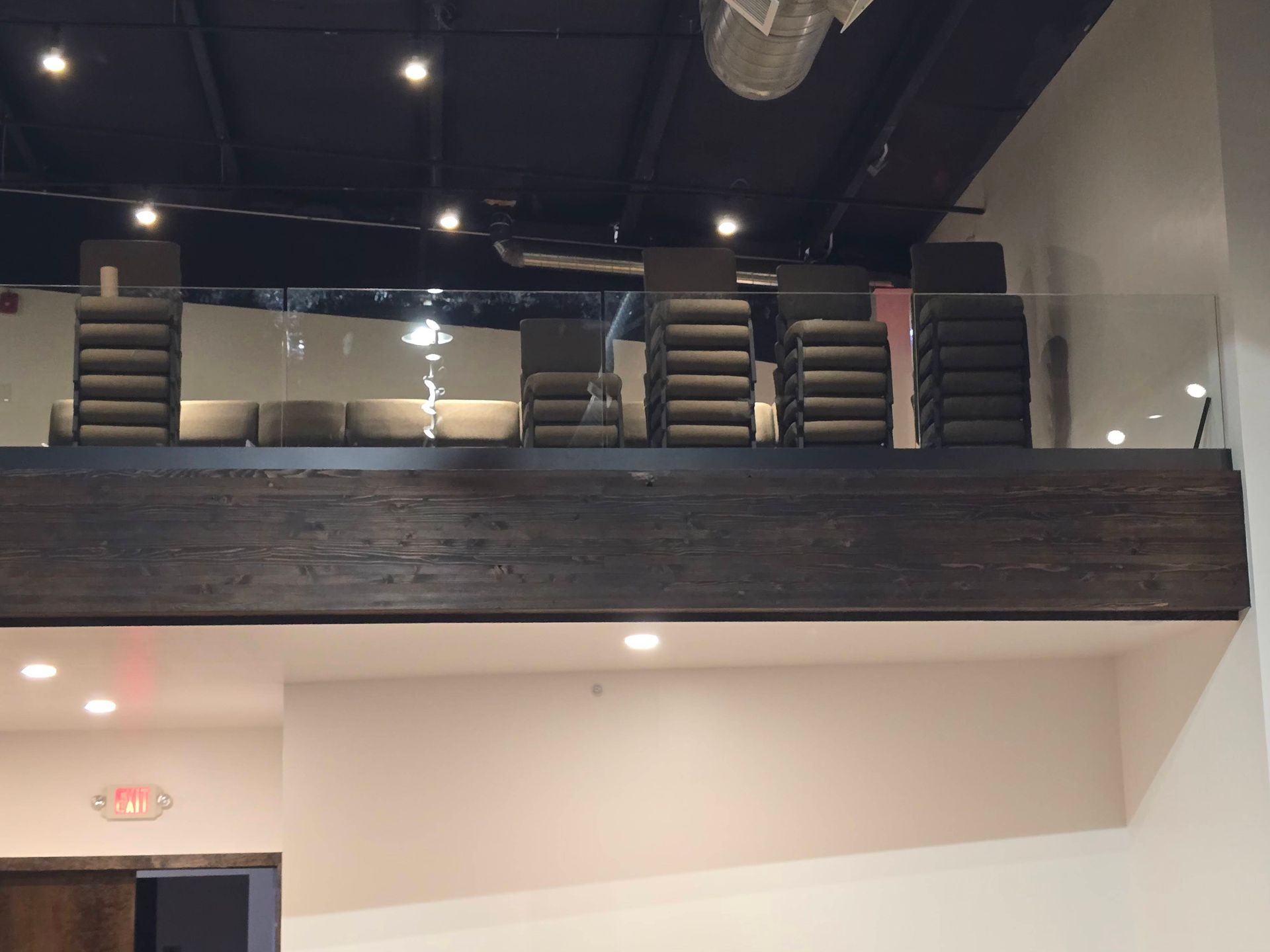 Modern loft interior with mezzanine seating, dark wood railing, and exposed ceiling lights