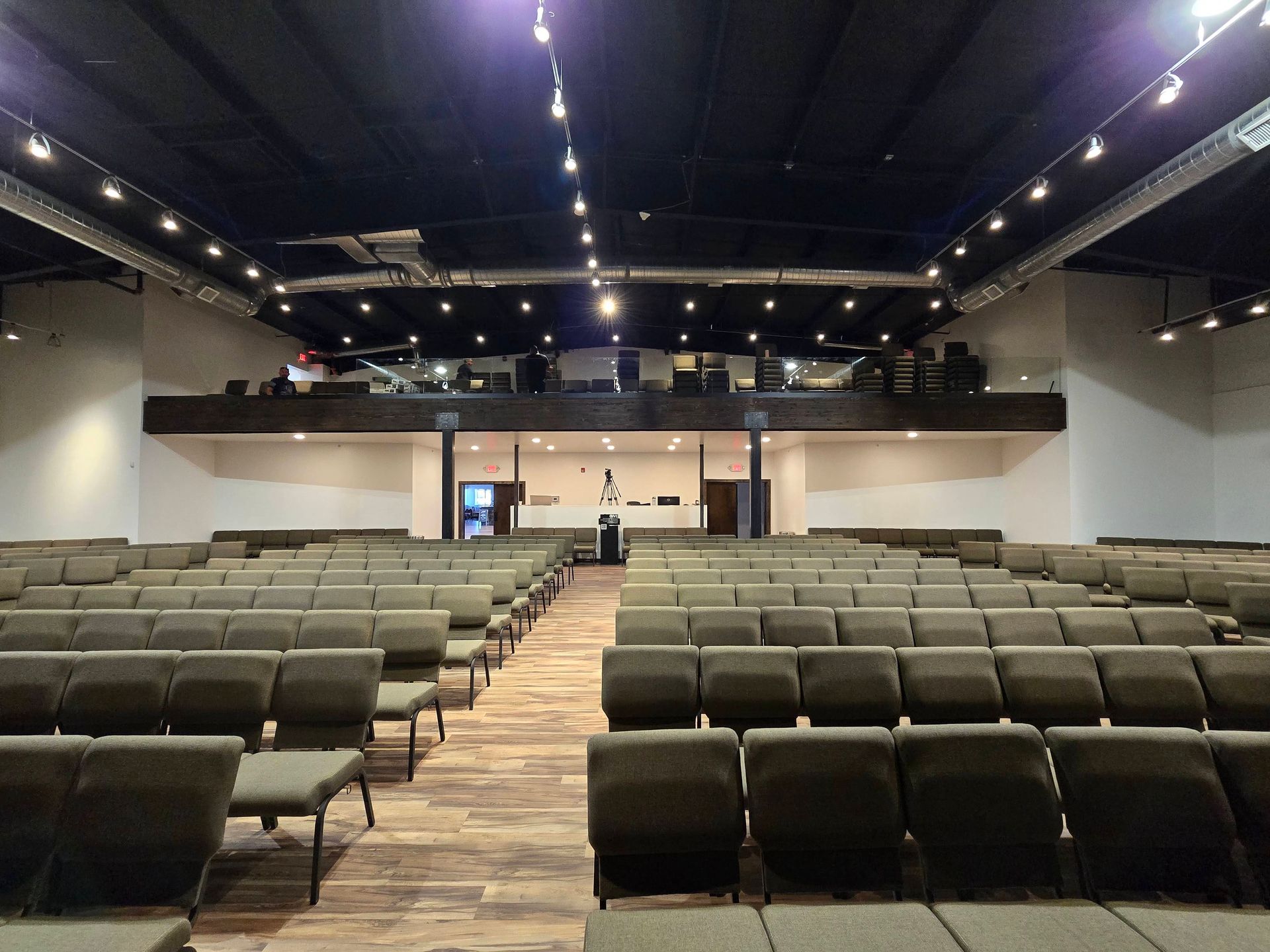 Empty auditorium with rows of green seats facing a stage and balcony under ceiling lights