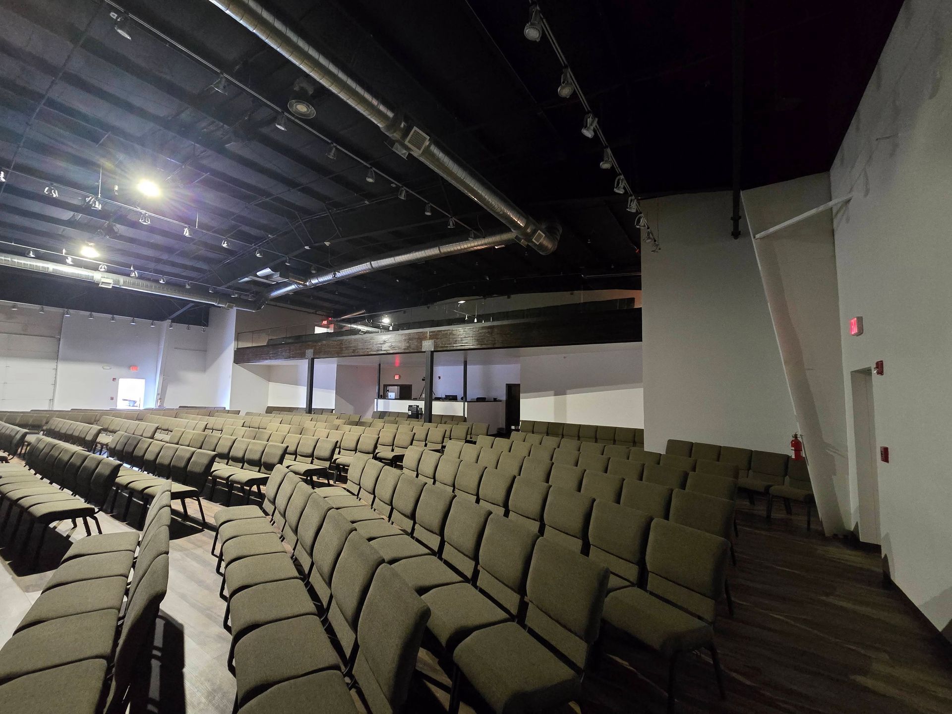 Empty auditorium with rows of beige seats, stage lighting, and a dark ceiling.