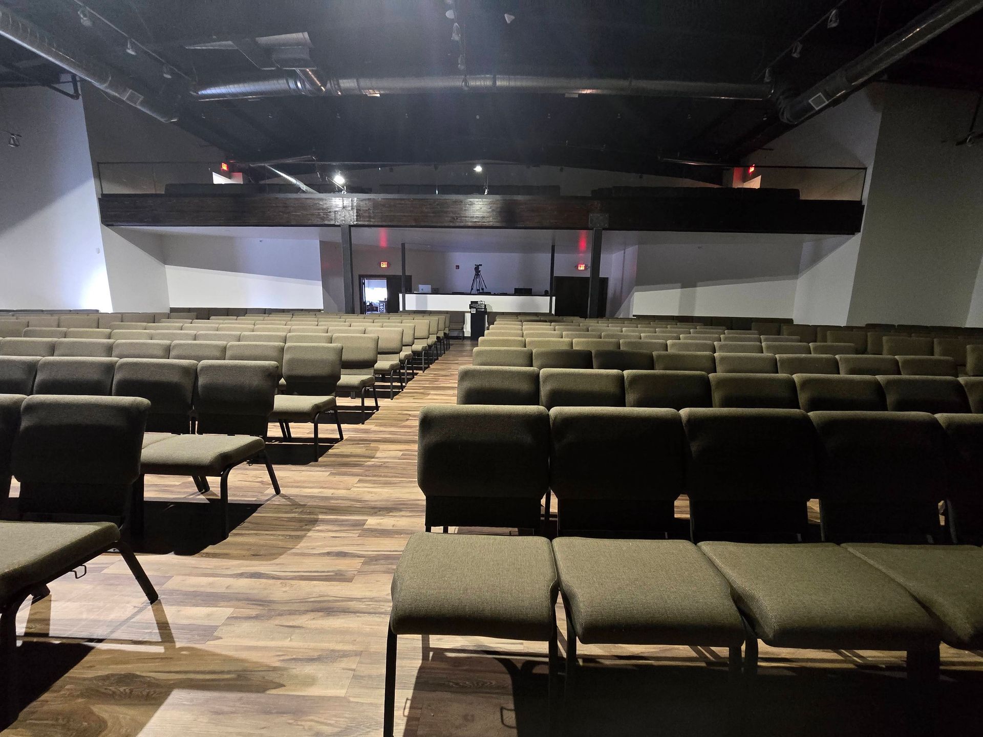 Rows of empty black chairs in a conference hall facing a stage with a podium.