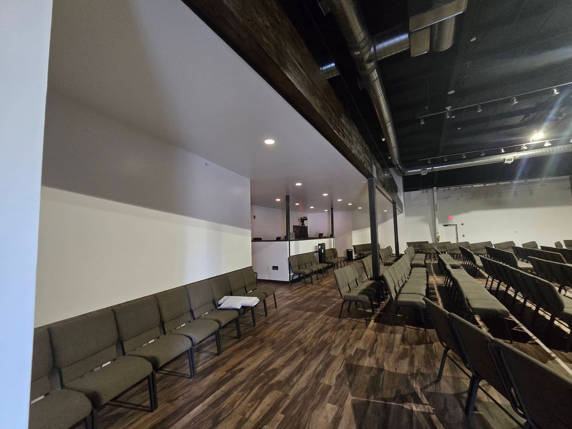 Empty indoor waiting area with rows of chairs, wood floor, and exposed ceiling beams