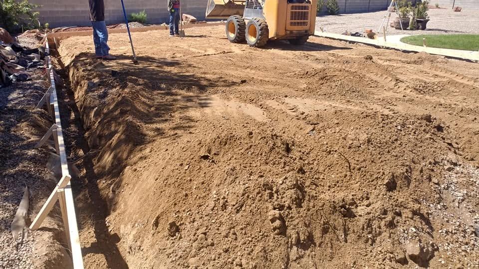 Construction equipment grading a dirt lot beside a sidewalk and street