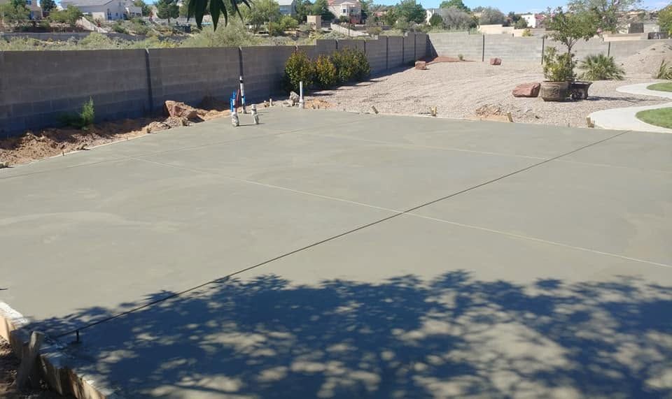 Empty concrete yard with a long wall, gravel area, and desert landscaping under bright sun.