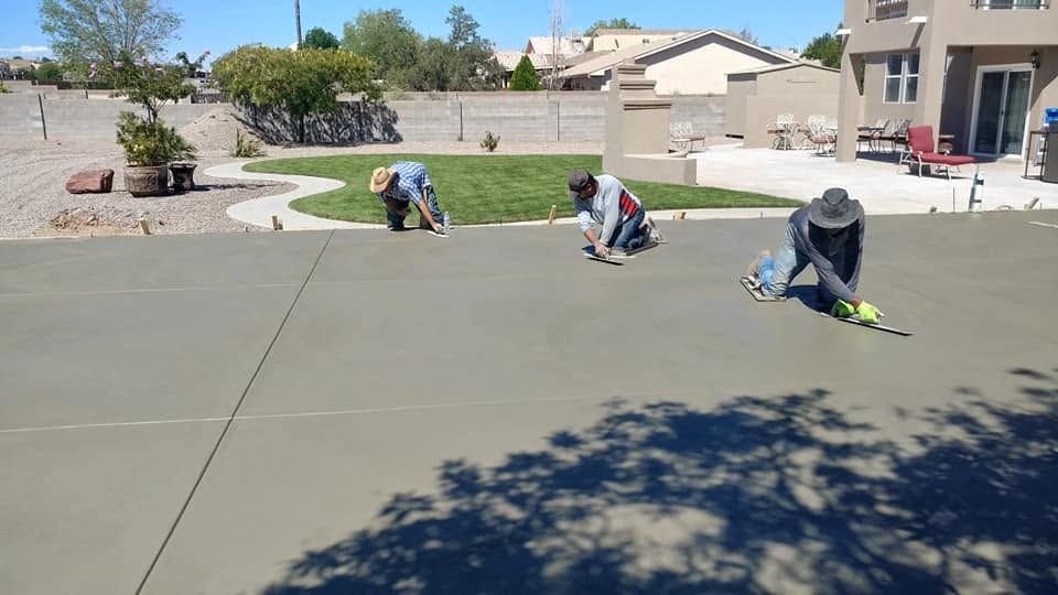 Three workers smoothing fresh concrete on a driveway in a sunny suburban neighborhood