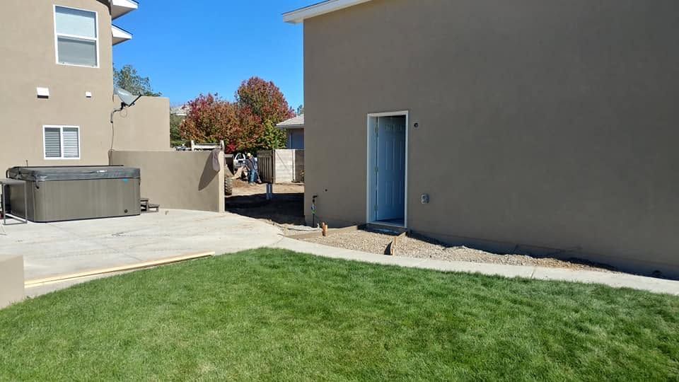 Backyard with green lawn, concrete patio, beige building, and a blue door under clear sky