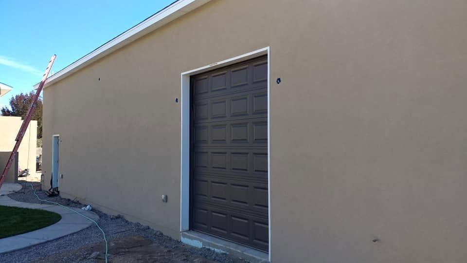 Beige building exterior with a dark garage-style door and concrete walkway.