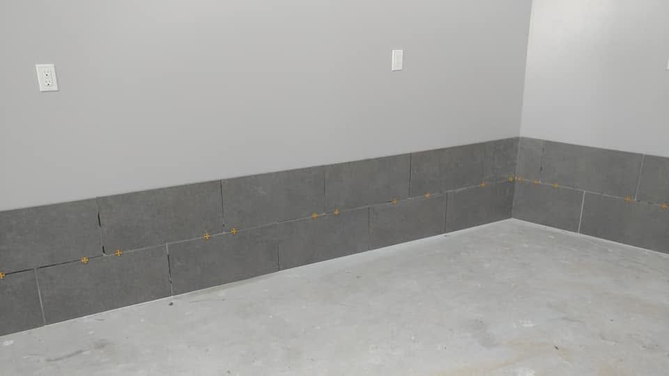 Empty gray room corner with cinderblock base and white walls; unfinished concrete floor and outlets.