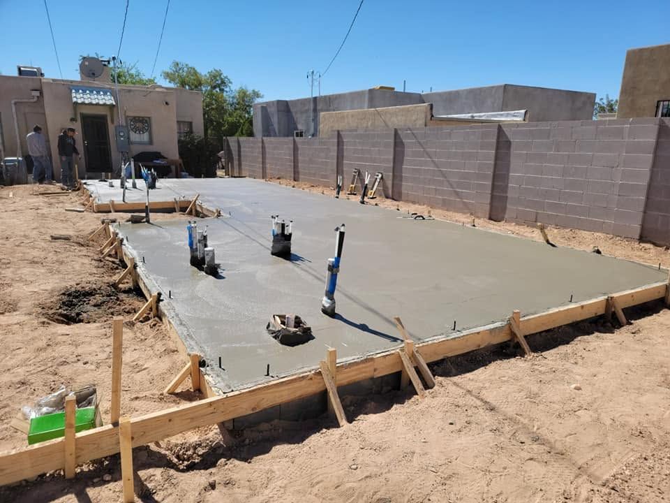 Fresh concrete slab being poured at a construction site, with pipes protruding and wooden forms along the edges