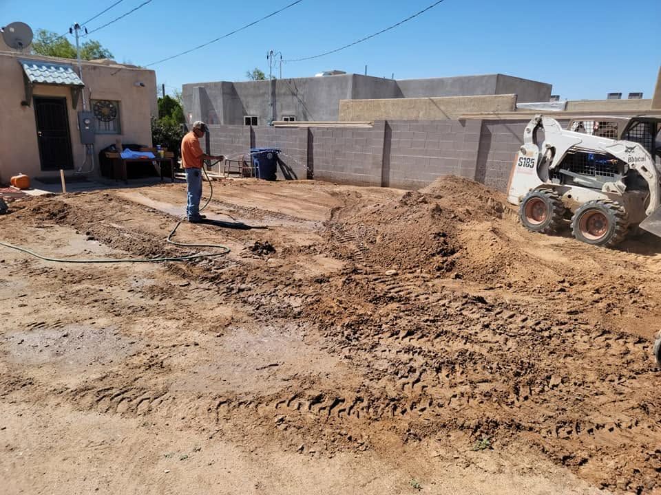 Construction site with dirt excavation, worker in orange vest, and skid steer beside a concrete wall