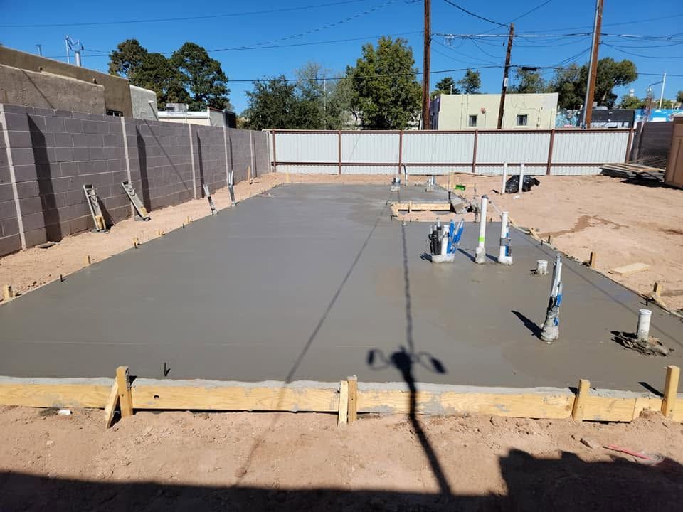 Concrete slab foundation under construction with plumbing pipes and forms in a backyard.