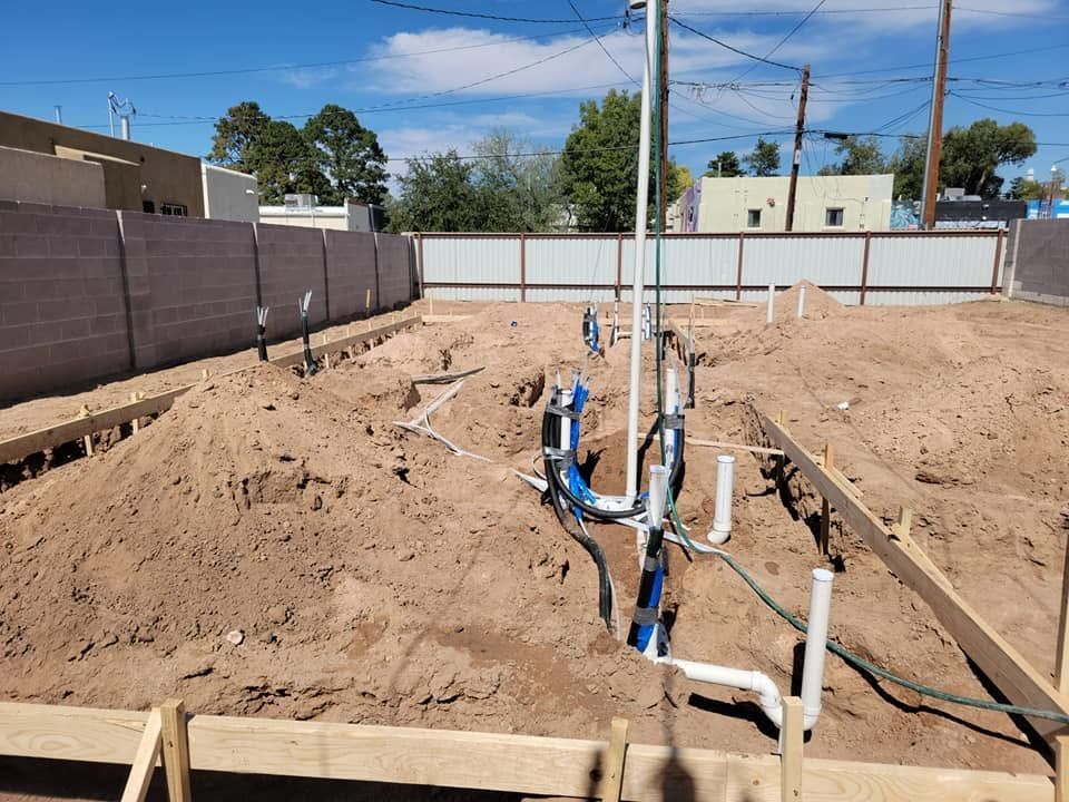 Utility trench with exposed PVC pipes and blue plumbing in a sandy construction site under a clear sky