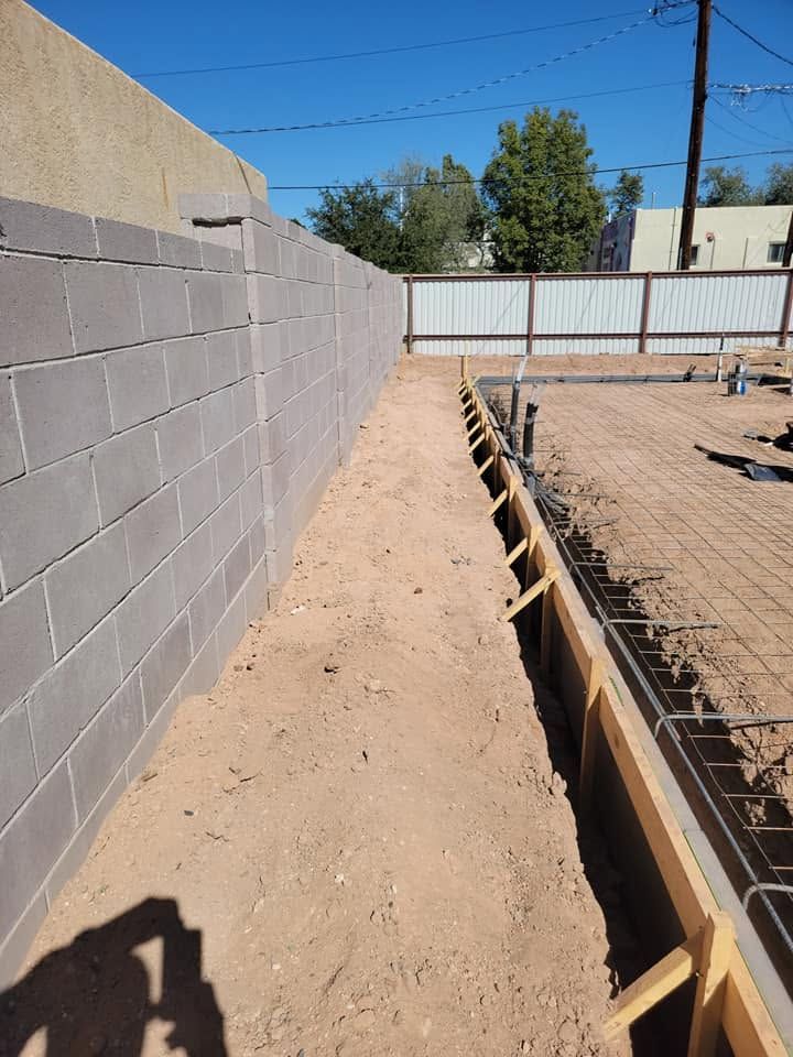 Narrow dirt path beside cinderblock wall and rebar foundation at a construction site