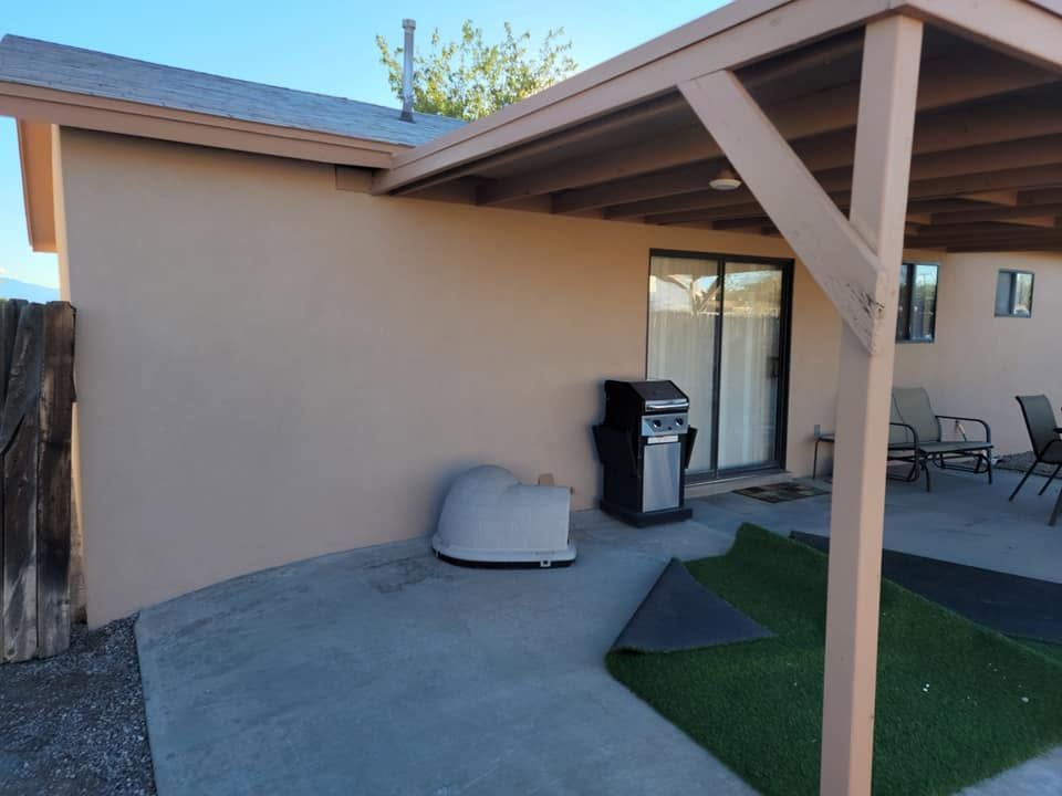 Patio with a grill, covered seating area, and artificial turf beside a tan house