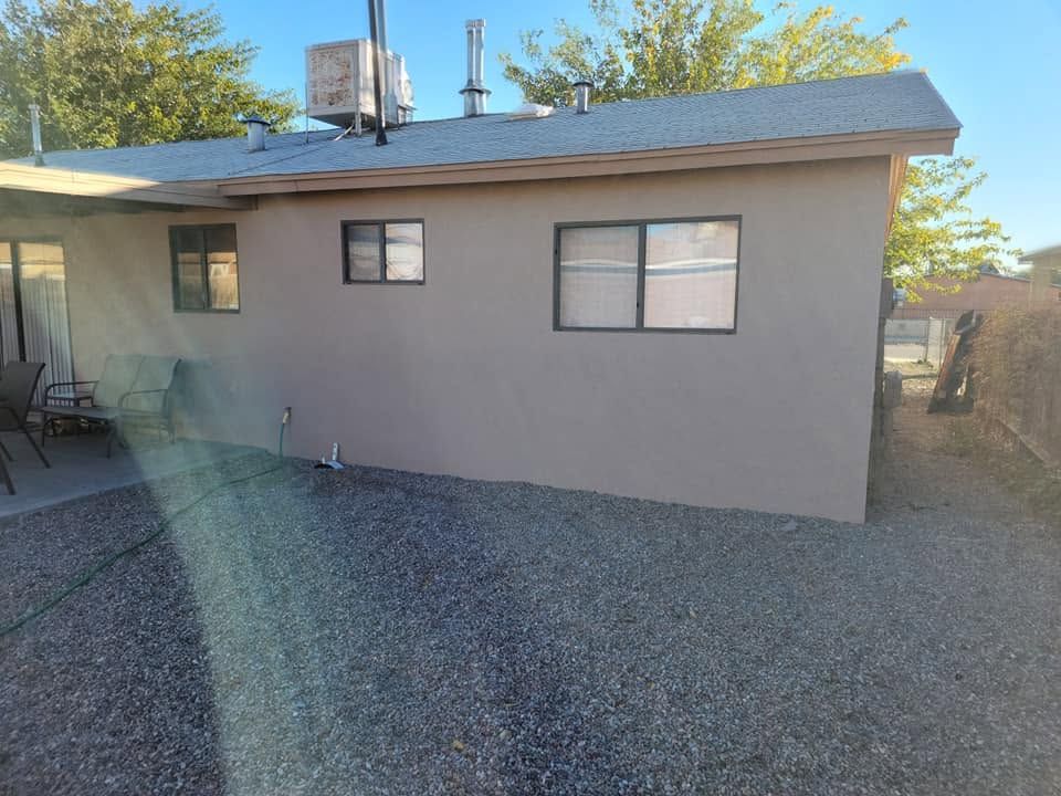 Single-story beige house with small windows and gravel yard under a clear sky