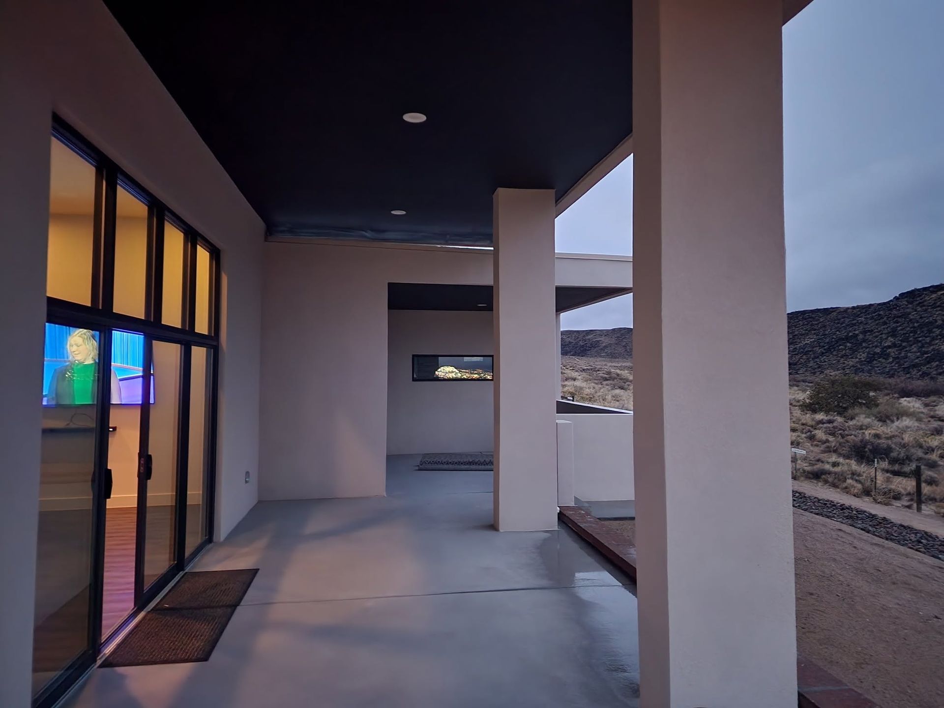 Covered porch with white columns, glass door, and desert mountain view at dusk