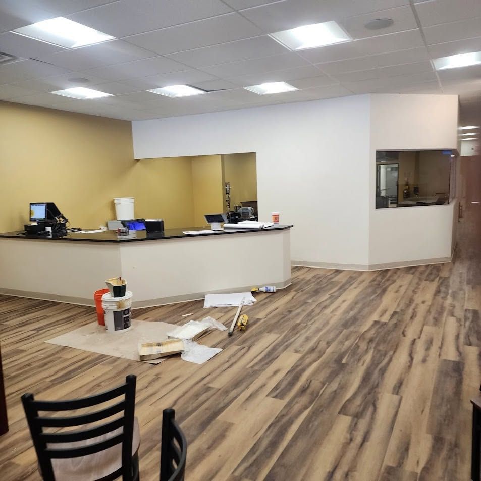 Empty office reception area with wood-look floors, white walls, counter, and scattered renovation materials