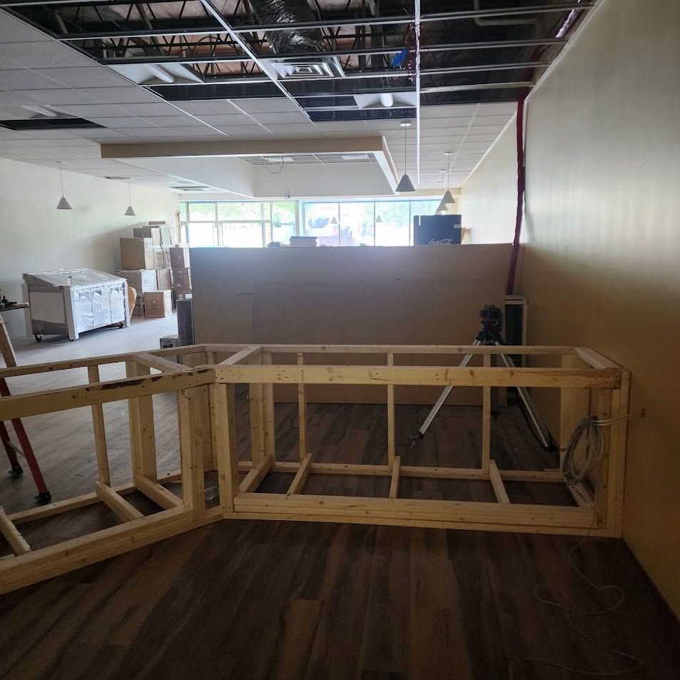 Empty room under renovation with exposed ceiling, wooden barrier in foreground, and furniture in the background