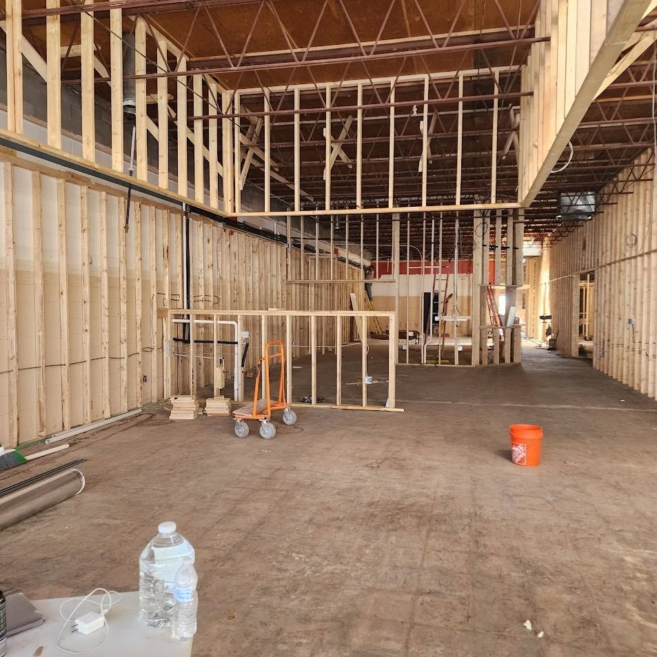 Unfinished interior construction site with exposed framing, tools, and buckets on a concrete floor.