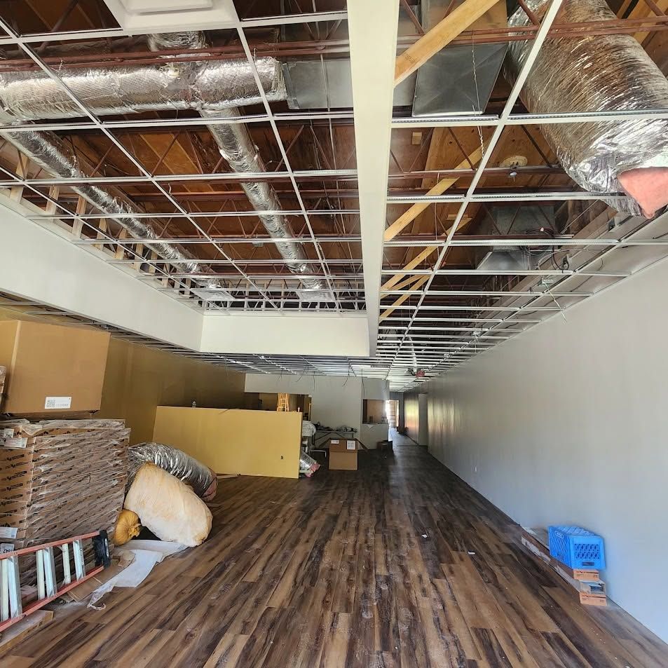Empty industrial room with exposed ceiling, wood floor, and boxes stacked along the left wall.
