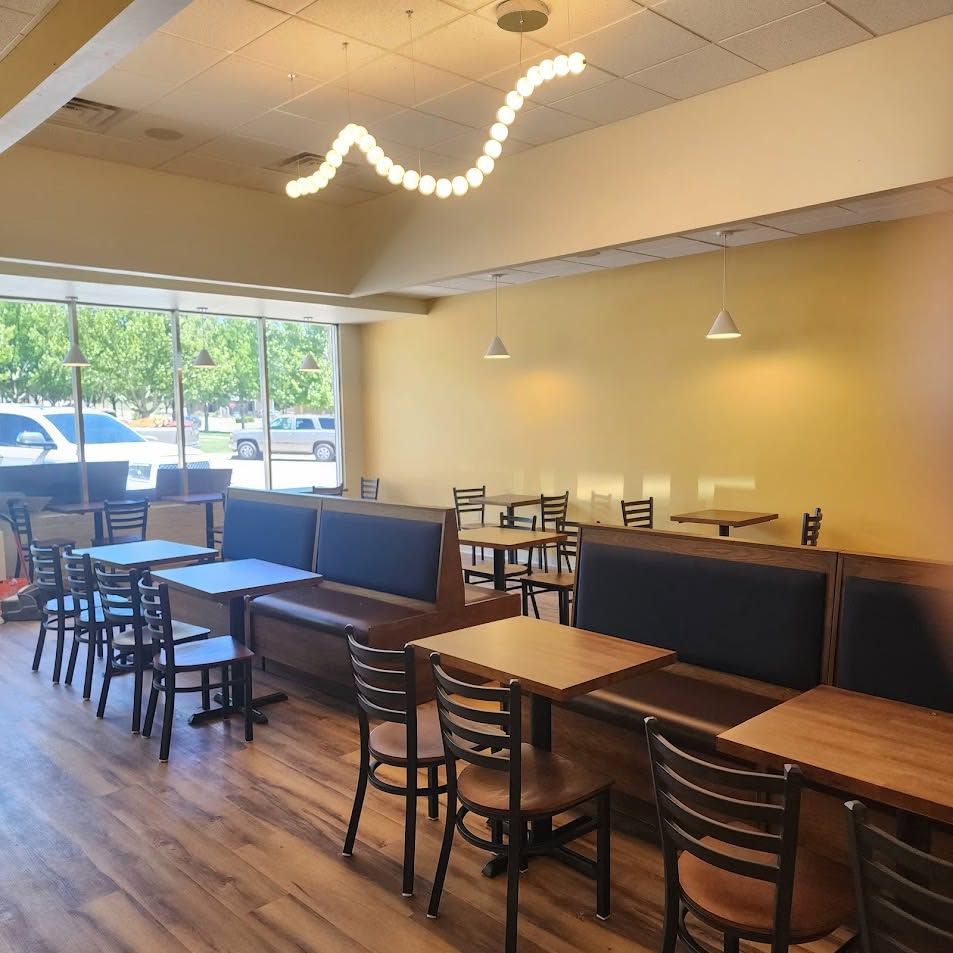 Empty café seating area with wooden tables, black chairs, and large windows in warm lighting