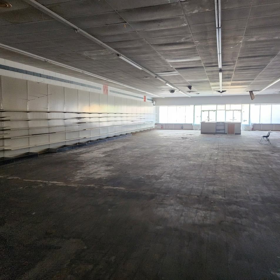 Empty retail store interior with bare shelves, concrete floor, and bright windows at the back