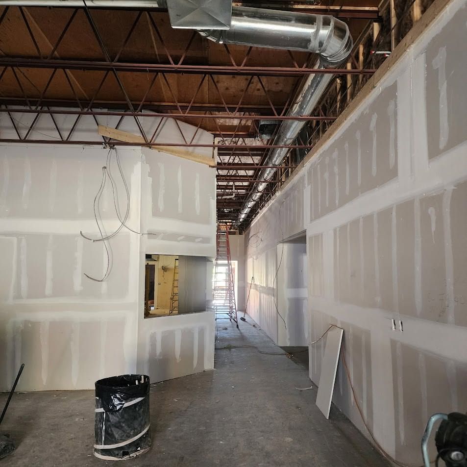 Partially finished hallway with drywall, exposed ceiling ducts, and construction debris in an unfinished building
