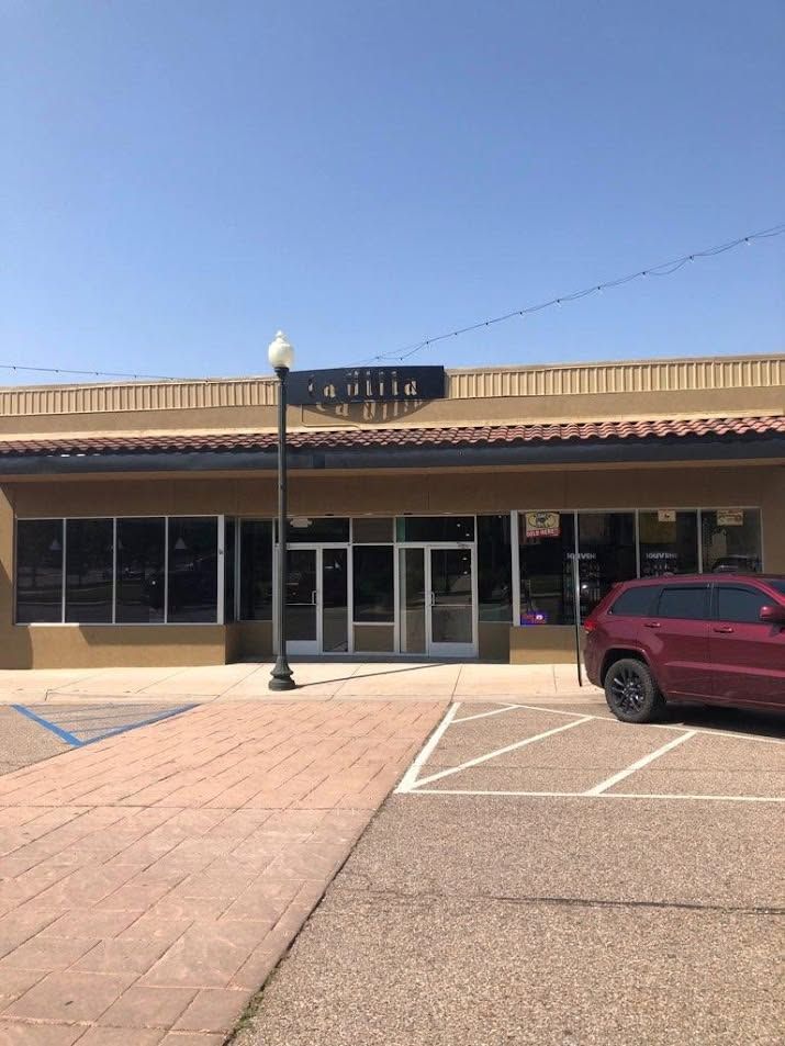 Small storefront with striped awning, glass doors, and a red SUV parked in front under a clear blue sky.
