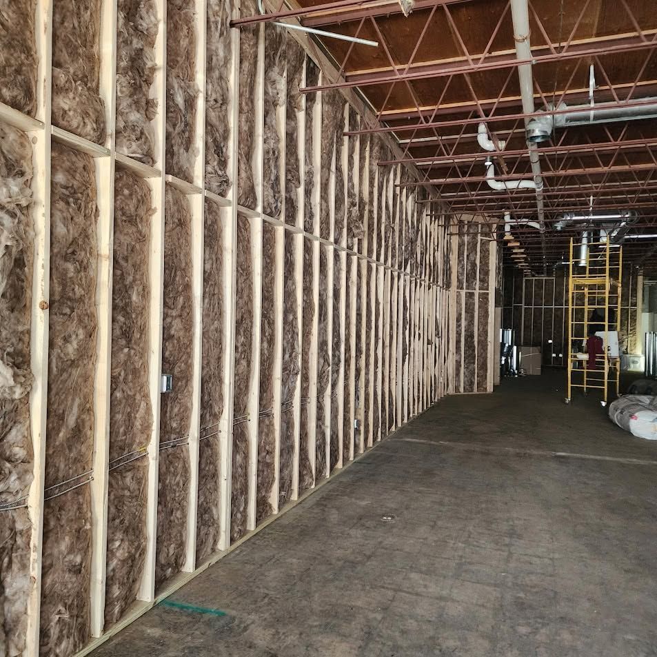 Interior of a construction site with exposed wooden framing, insulation, and a dark concrete floor.