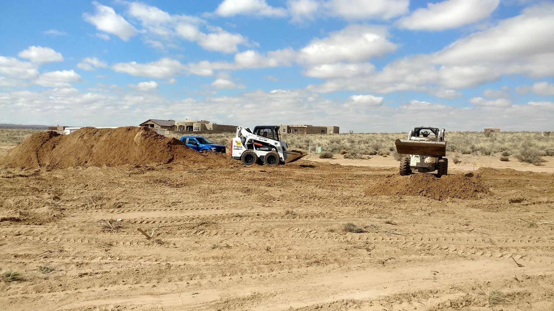 Bulldozer and dump truck at a dusty construction site under a blue sky