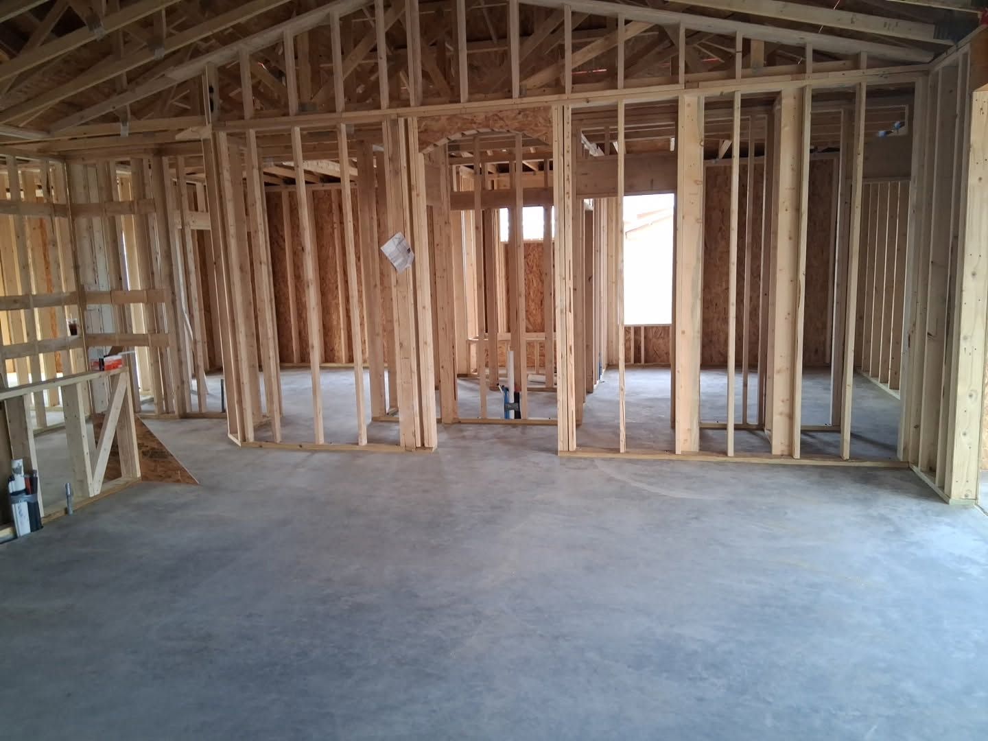 Unfinished wooden house interior with exposed framing, concrete floor, and roof trusses.