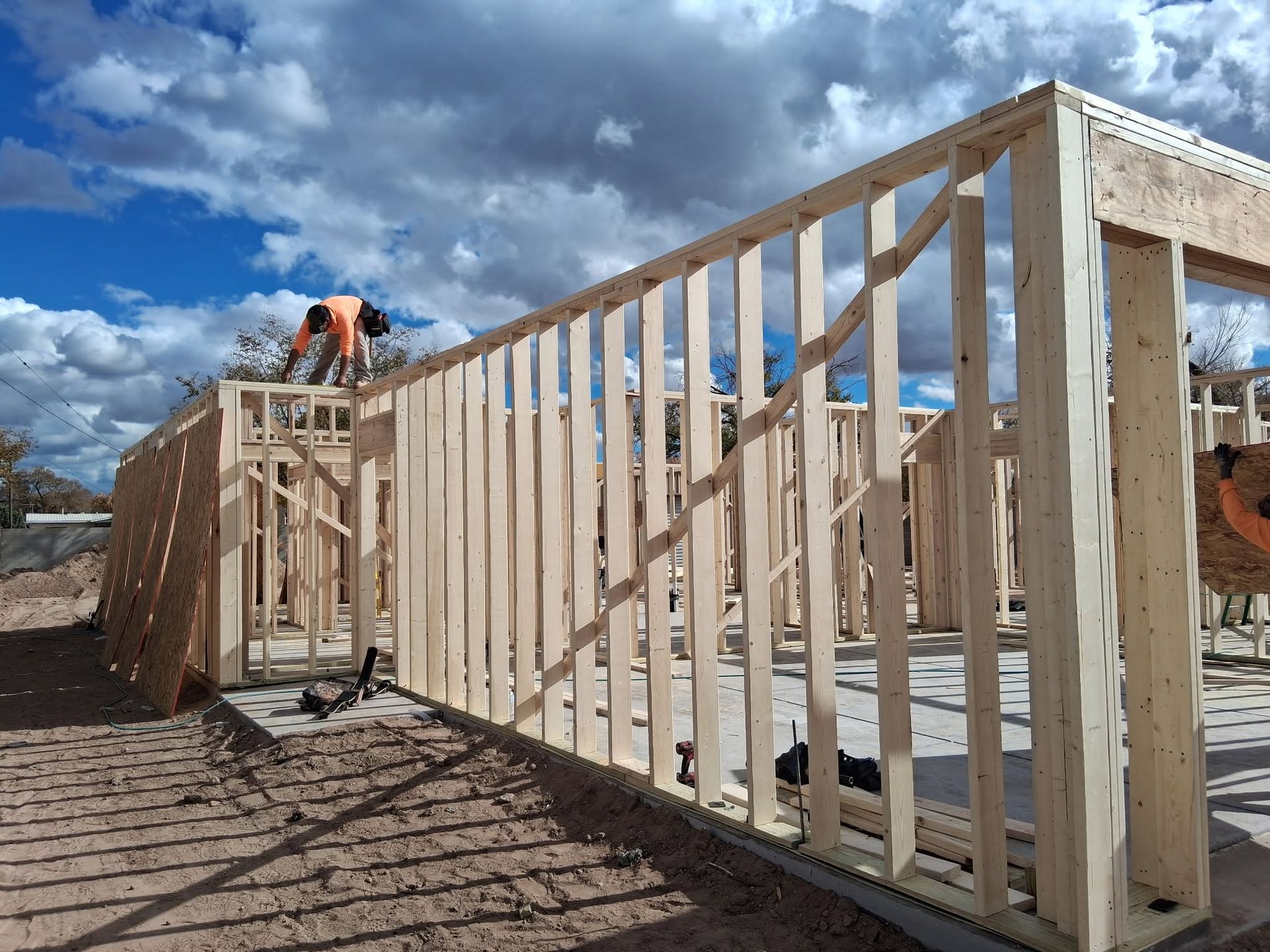 Workers framing a house with wooden studs under a partly cloudy sky