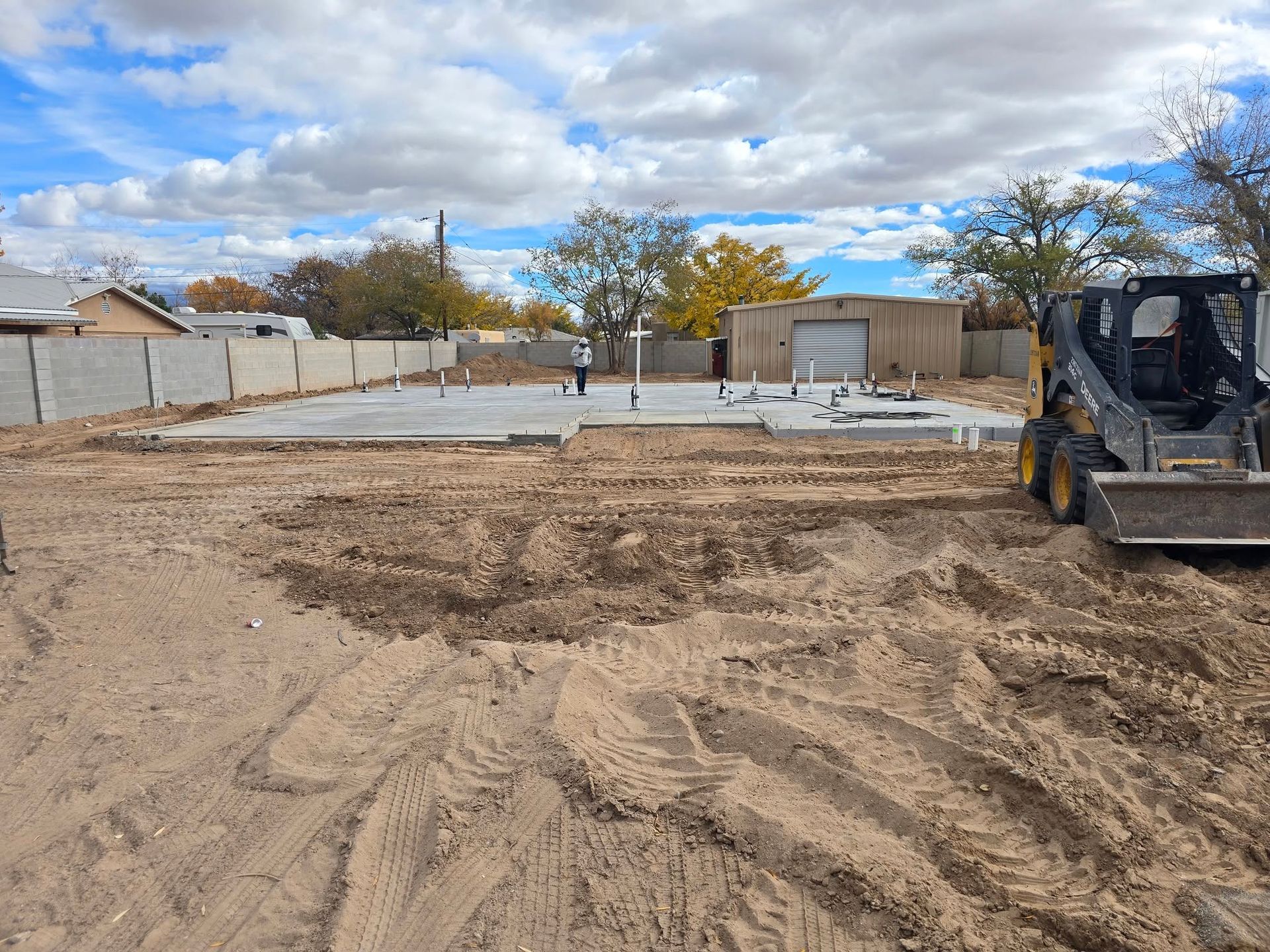 Construction site with bulldozer grading dirt under a cloudy sky in a fenced residential area