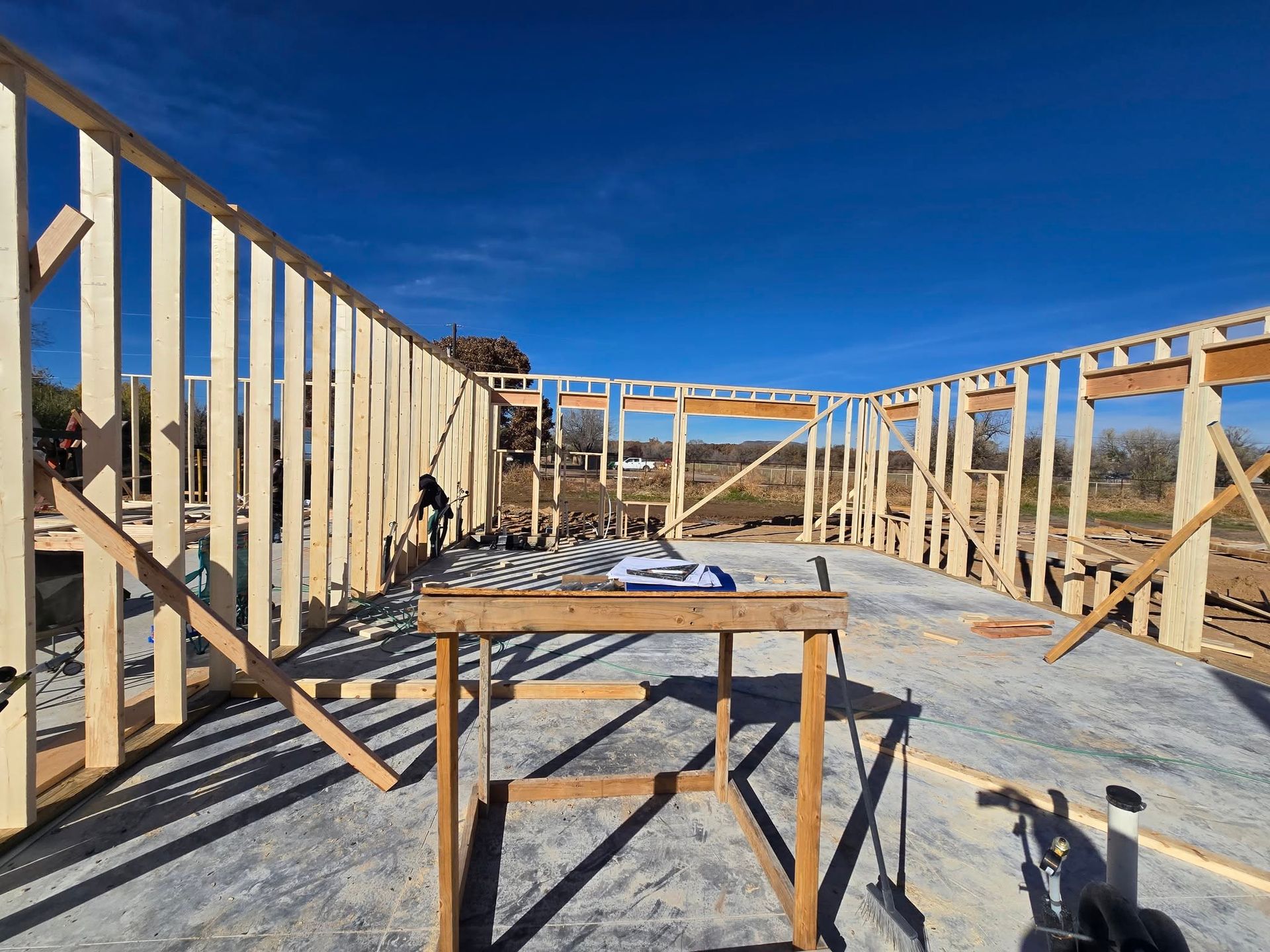 Wood-framed house under construction with a table saw on a rooftop under a blue sky