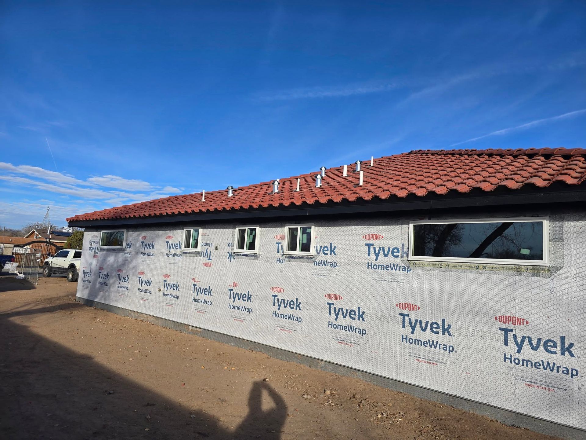 House under construction with Tyvek wrap, red tile roof, and blue sky overhead