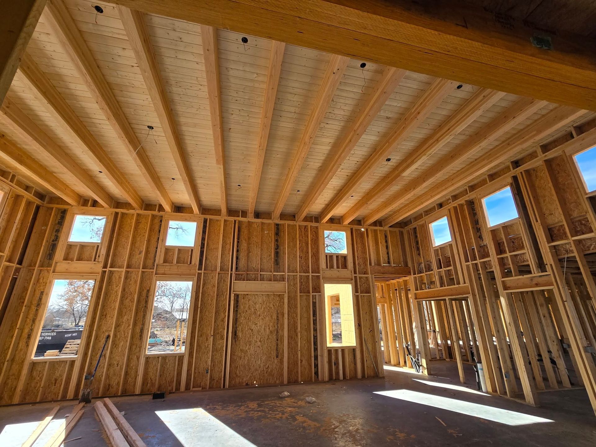 Interior of a wood-framed house under construction with exposed studs, windows, and sunlight on the floor