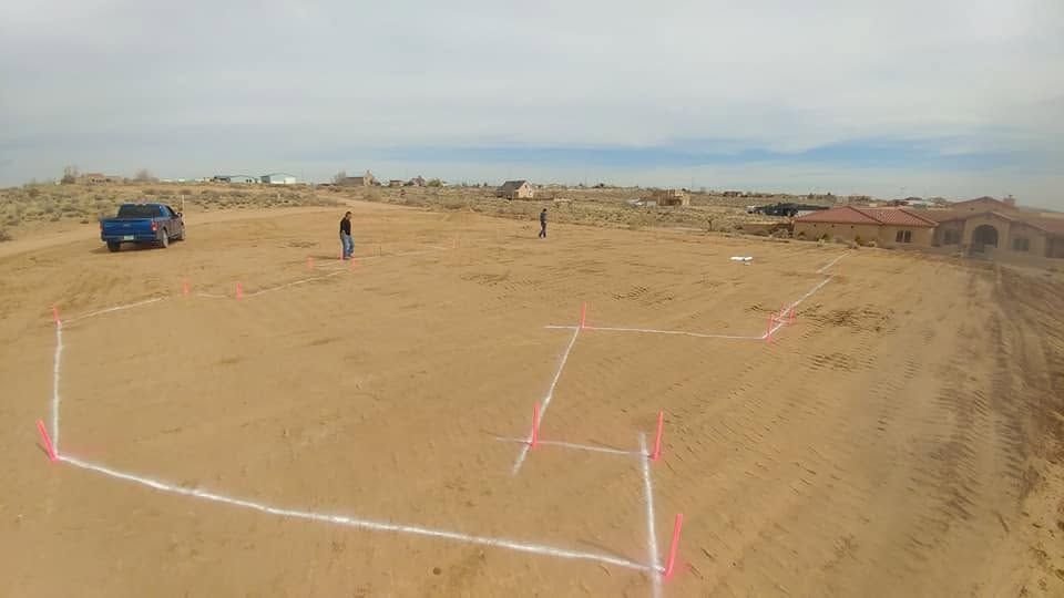 Marked sandy lot with a blue car and a few people in the distance under a hazy sky