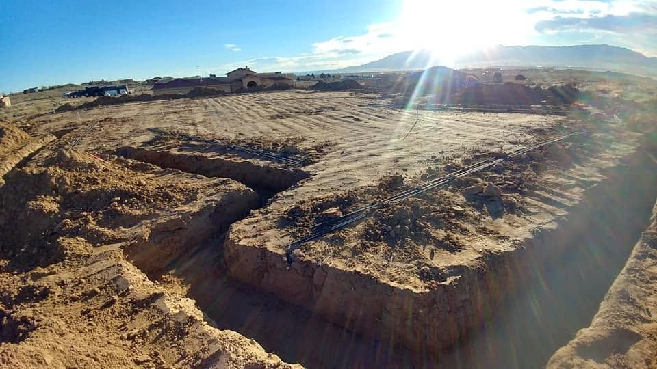 Wide barren construction site with excavated earth and bright sun flare over distant hills