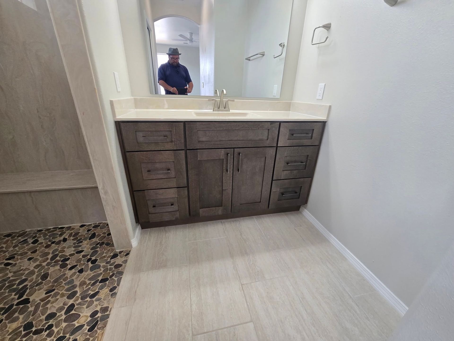 Bathroom with dark wood vanity, white countertop, and mosaic tile floor, with a person reflected in the mirror.