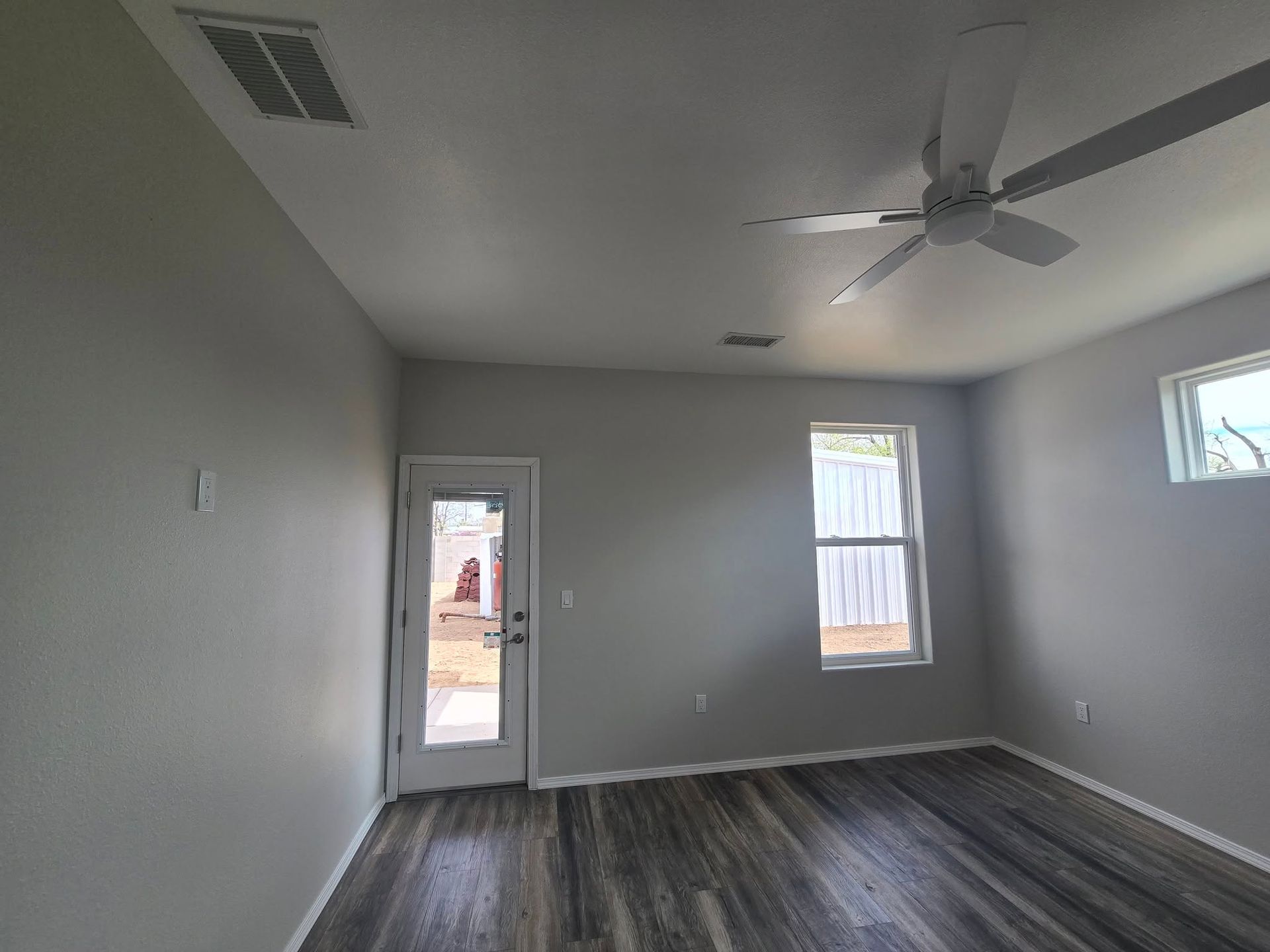 Empty gray bedroom with dark wood floors, a ceiling fan, and two windows near a doorway.