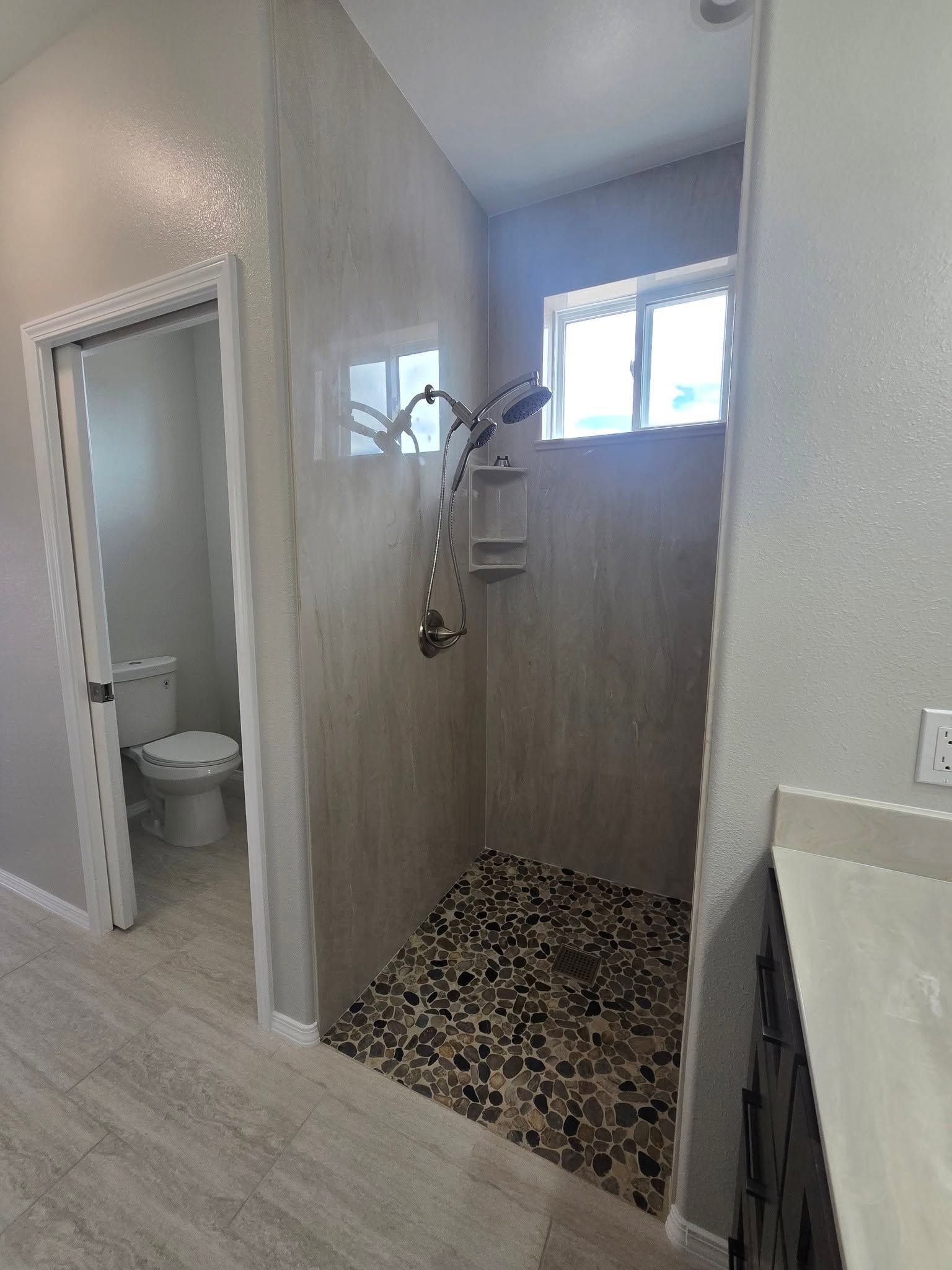 Small bathroom with open shower stall, tiled floor, and toilet visible through a doorway.