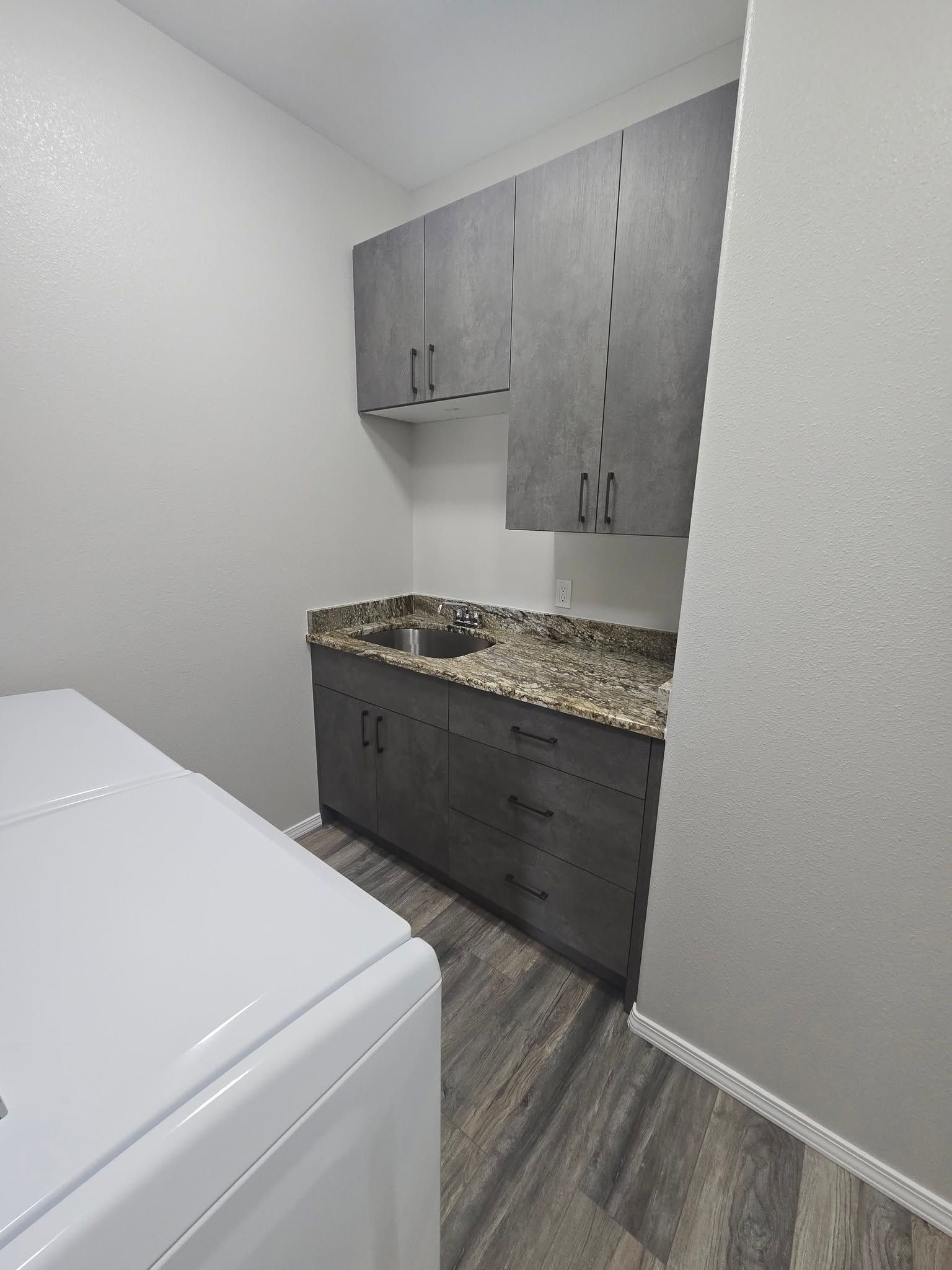 Small utility room with gray cabinets, granite countertop, and a white washer in the foreground.